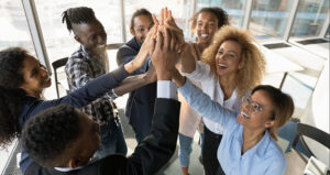 A circle of diverse colleagues join hands in air to celebrate success, effective teamwor