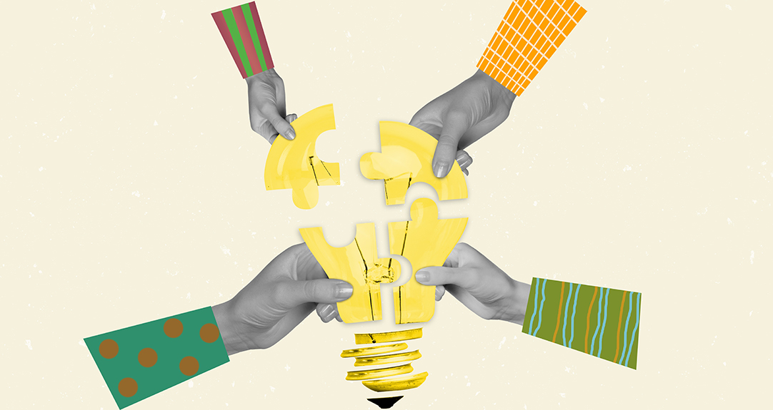 Four hands collaborate by putting together a puzzle of a lightbulb.