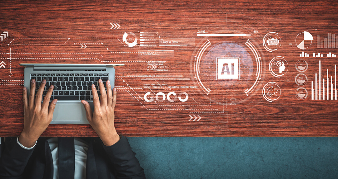 Seen from above, a man’s hand hover over a laptop keyboard while white business-related graphics spread over his work surface.