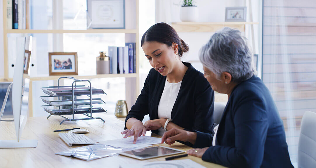 Two women in an office examine detailed paperwork.