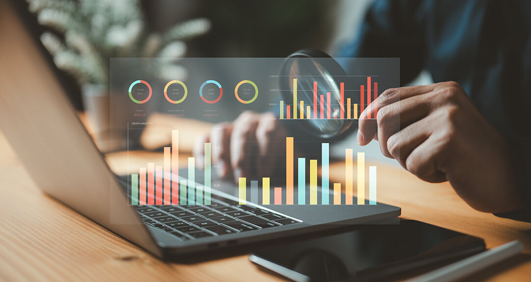 An accounting-style graphic floats above a laptop keyboard. A man holds a magnifying glass behind the graphic.