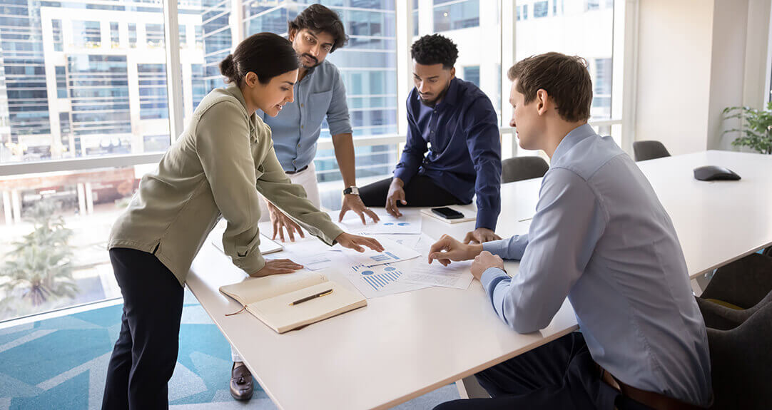 Four people confer around a table in a bright, modern office.