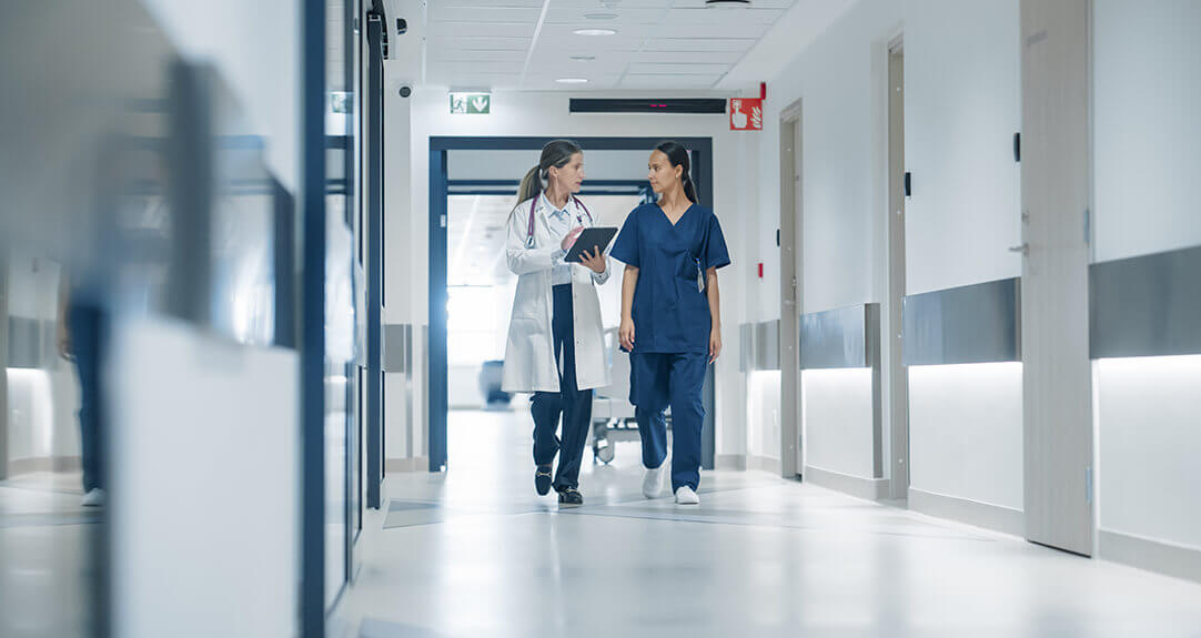 Two clinicians walk down a hospital hallway.