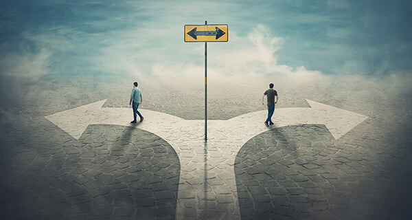 A path divides into two pathways—one to the right and one to the left. The same man, in slightly different outfits, walks on each of the diverging paths.