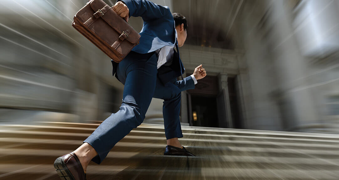 A man with a briefcase rushes toward the entrance of an official-looking bank or government building.