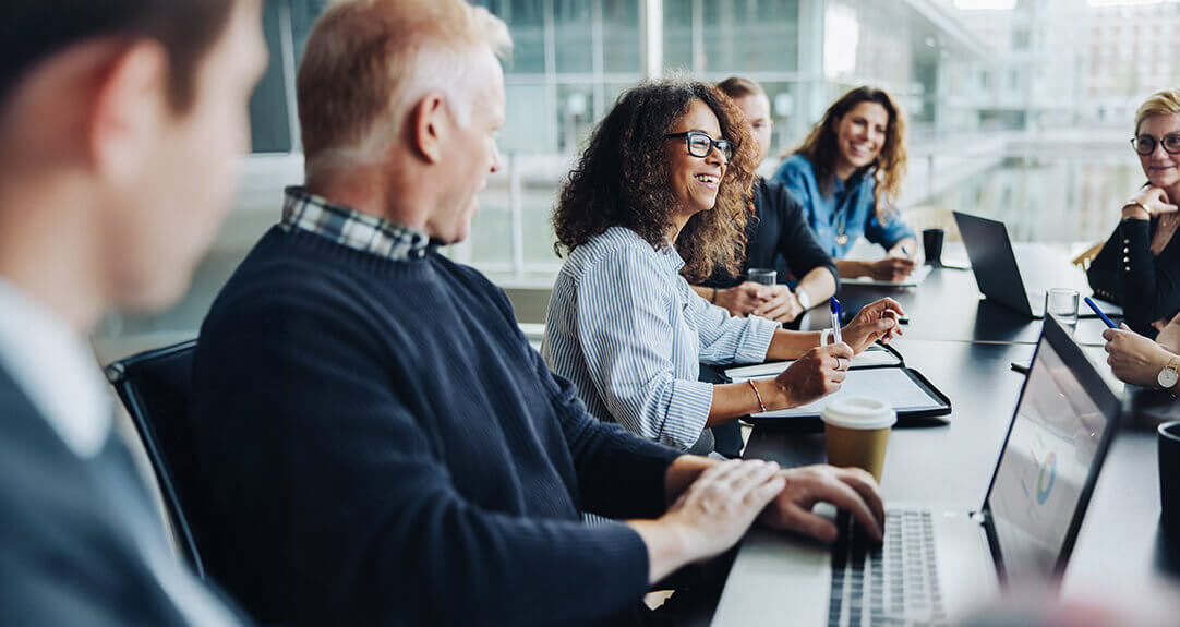 A group of friendly, engaged professionals sits around a conference table.