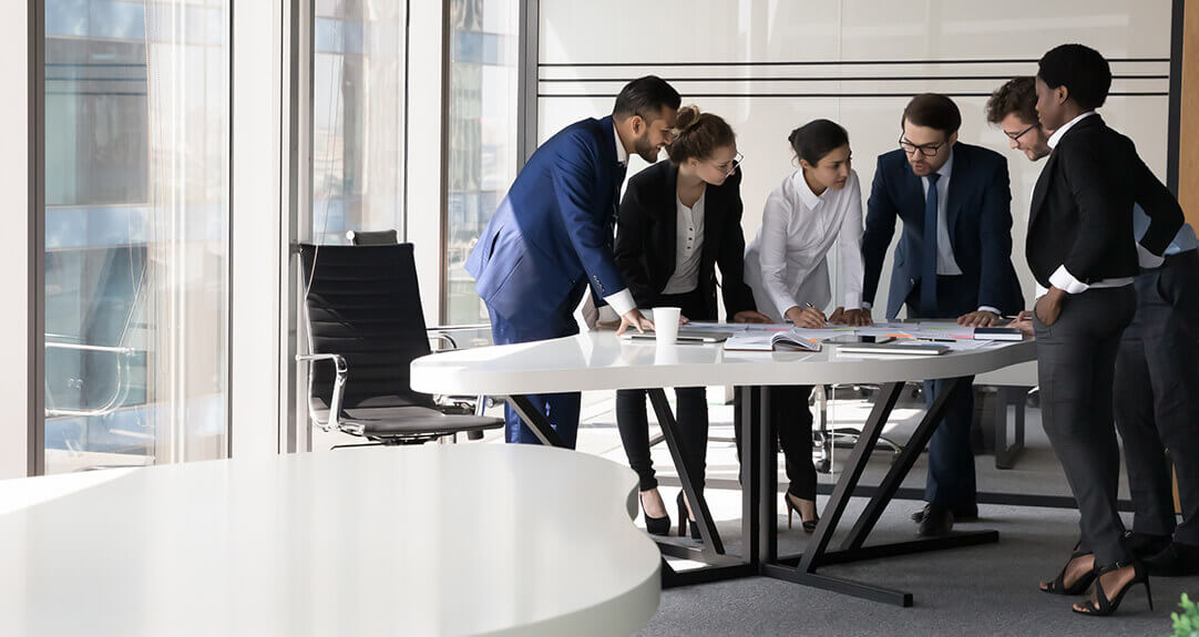 Men and women in business attire discuss a project in an office conference room.